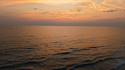 Golden sunset paints the sky with warm hues over a tranquil ocean, small waves gently rolling towards the shore, creating a serene and picturesque seascape
