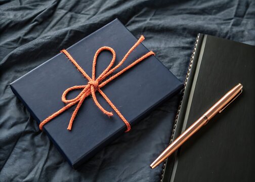Navy gift box tied with orange twine next to a notebook and elegant pen