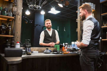 Experienced hairdresser preparing place for the next customer. Barber cleaning table after last client. Handsome man looking in mirror and smiling.