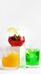 Three glass tumblers with red, yellow, and green lemonade on white background. Cold summer drinks with ice and condensation drops on glass surface. Refreshing for hot weather and restaurant