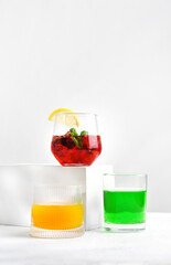 Three glass tumblers with red, yellow, and green lemonade on white background. Cold summer drinks with ice and condensation drops on glass surface. Refreshing for hot weather and restaurant