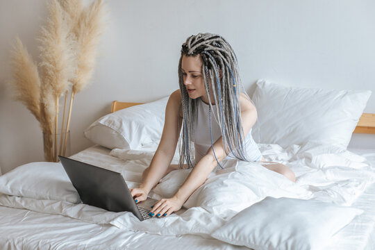 Young woman communicating at computer, laptop in white bed.