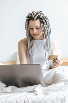 Happy woman shopping at computer, laptop in white bed.