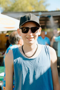 Young man smiling wearing sunglasses and baseball cap outdoors