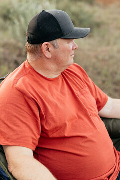 Middle-aged man in cap relaxing outdoors at forest campsite