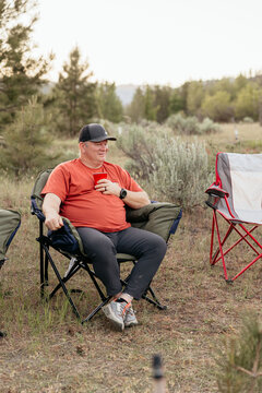 Middle-aged man sits with drink in hand at peaceful campsite
