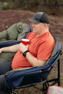 Camper relaxing in folding chair, enjoying nature with red cup