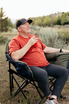 Man in 50s relaxing with drink while camping in forest setting