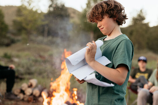 Young boy reading by the bonfire during summer camp