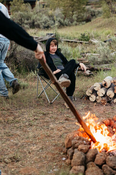 Teen relaxing in camping chair near fire pit with logs and flames