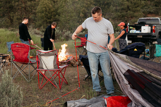 Friends setting up campsite with tent and campfire