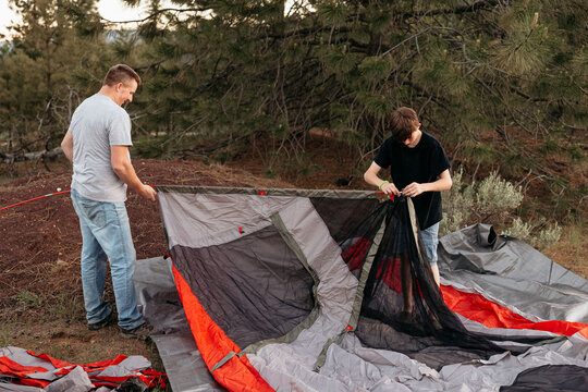 Man and teen assembling tent together in wooded campsite area