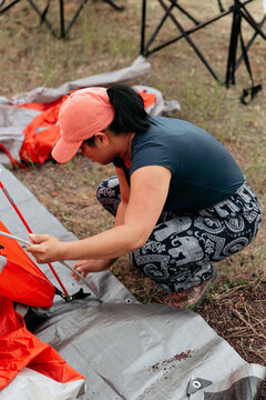Camper putting tent poles into a red tent on a campsite