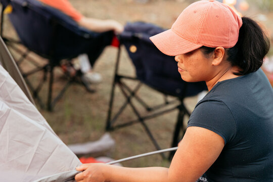 Woman setting up tent at campsite wearing coral cap and t-shirt