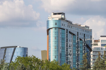 A modern high-rise building in the center along with other buildings and trees nearby