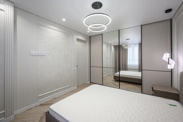 Modern bedroom with mirrored closet, ring chandelier, and textured walls. Neutral color palette