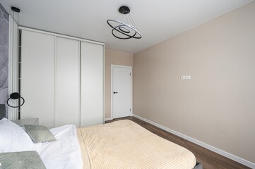 bedroom interior with neutral tones, featuring a bed, wardrobe, and modern lighting