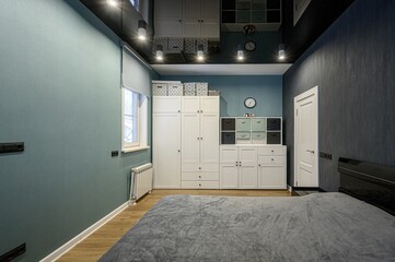 modern bedroom with a gray bed, light blue walls, white cabinets, and dark blue accent wall. Track...