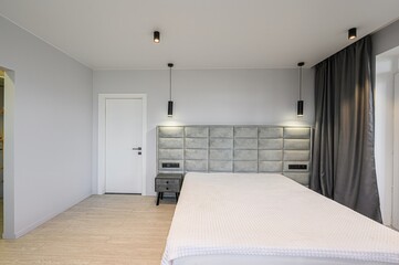 Modern bedroom featuring a bed with a gray headboard, white bedding, gray walls, and minimalist black lighting fixtures