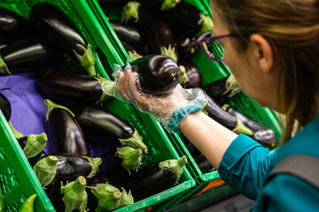 A person carefully selects a shiny eggplant from a crate, highlighting the process of choosing...