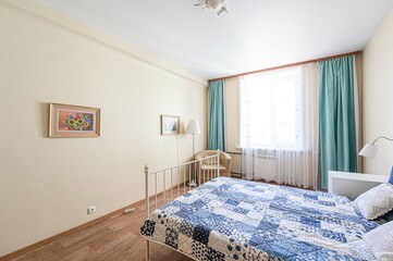 cozy bedroom features a blue patchwork quilt on a bed. Walls are light beige, adorned with framed...