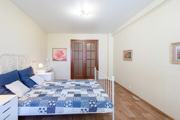 bright bedroom showcases a bed with a blue patchwork quilt, white frame, and matching furniture....
