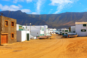 Charming coastal village of Famara, Lanzarote, with whitewashed houses and fishing boats resting on...