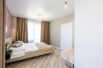 Cozy bedroom featuring a bed with neutral tones, complemented by warm lighting, curtains, and...