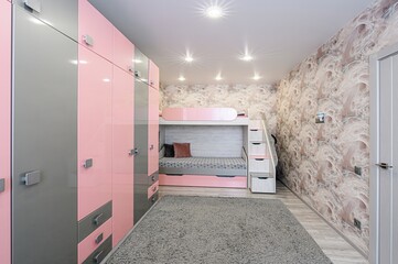 tidy kids' room with a pink and gray wardrobe, bunk bed, and a plush gray rug. Soft, patterned...