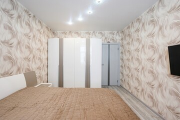 bedroom featuring a double bed with a quilted brown cover, patterned wallpaper, a white wardrobe,...