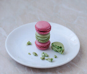 Colorful macarons stacked on white plate with crumbs – elegant French dessert