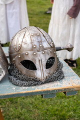 Four medieval-style helmets are displayed on a rustic table during a historical reenactment event, showcasing various armor styles.