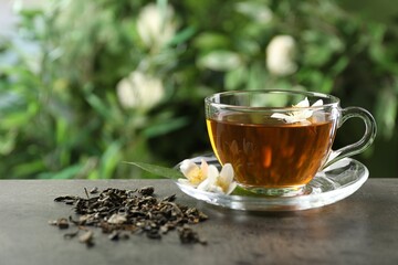 Aromatic jasmine tea in glass cup, brew and flowers on grey table outdoors, closeup