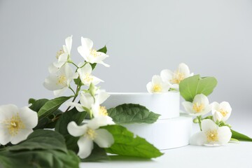 Beautiful jasmine flowers with leaves on light background, closeup