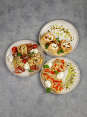 Gourmet dinner or lunch. Three plates with dishes of thin pancakes stuffed with red caviar, mushrooms and prosciutto on a gray background. Restaurant menu. Top view.