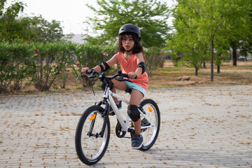 Fototapeta premium Girl riding a bicycle wearing helmet and protections in a park