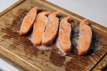 Raw salmon cut into steaks lies on a wooden cutting board in the kitchen with a slice of lemon.