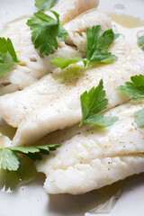 Dettaglio macro di filetto di pesce bianco condito con olio e prezzemolo fresco