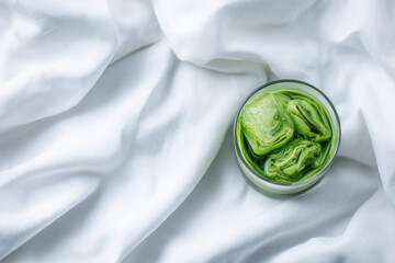 Obraz premium Iced matcha in transparent glass on white fabric, refreshing green tea beverage with ice cubes, minimal style, top view, relaxing mood