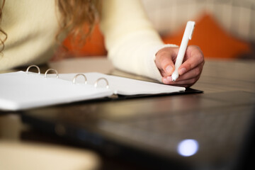 Woman hand writing in notebook during watching lesson on laptop, female in yellow sweater with pen...