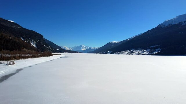 Lake Reschen - Vinschgau, South Tyrol - rising aerial photograph over the frozen lake with a view of the Ortler mountain range