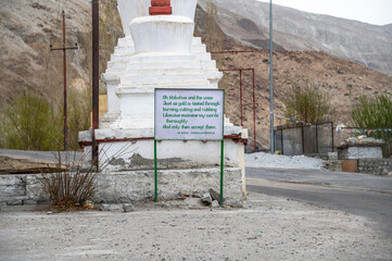 Scenic road intersection in Ladakh with inspirational Buddha quote signboard against a mountain...