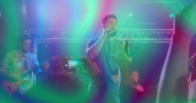 Vocalist stepping to mic under swirling lights at concert while smartphones beer bottles raising