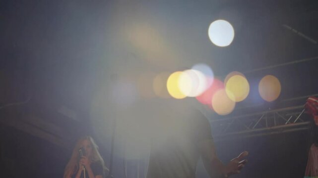 Lead singer stepping center stage and gripping mic for chorus while colored lights moving overhead