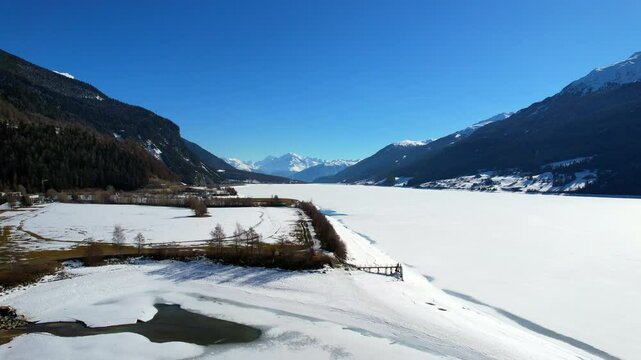 Lake Reschen - Vinschgau, South Tyrol - Aerial view of the frozen white lake with a view of the Ortler mountain range
