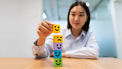 Woman placing yellow happy face cube on stack of colorful emotion blocks