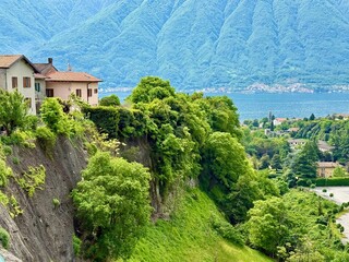 Hillside village in Lenno Ossuccio, with colorful houses, winding stone alleys, lush greenery, steep cliffs and panoramic view of church tower above the forested valley