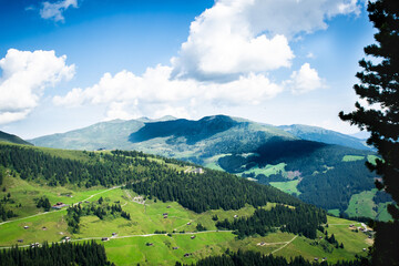 A breathtaking panoramic view of vast green mountain slopes, dense forests, and quaint scattered...