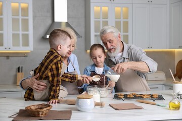 Grandparents and their grandkids cooking together at white marble table in kitchen