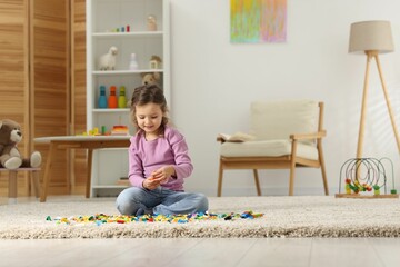 Cute girl playing with building blocks on floor at home. Space for text